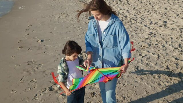 Mother and her son playing with kite on beach near sea. Camera moving around them