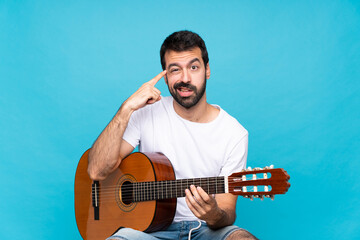 Young man with guitar over isolated blue background making the gesture of madness putting finger on the head
