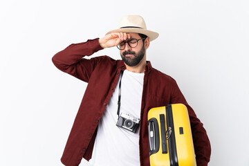 Traveler man man with beard holding a suitcase over isolated white background with tired and sick...