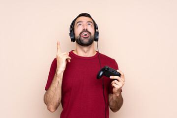 Man playing with a video game controller over isolated wall pointing up and surprised