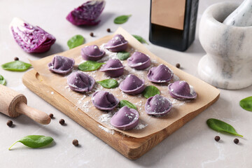 Purple dumplings on kitchen board, cabbage and spices on light background