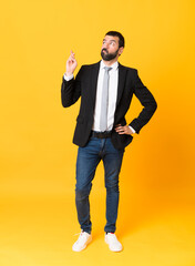 Fototapeta na wymiar Full-length shot of business man over isolated yellow background with fingers crossing and wishing the best