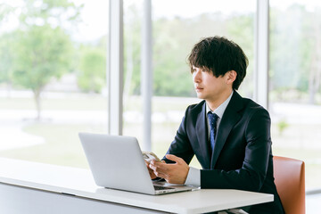 パソコンをスマホを両方使う若いアジア人ビジネスマン
