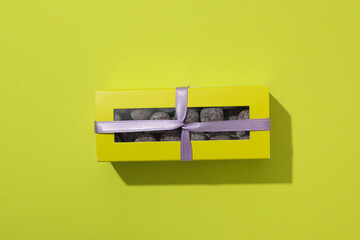 Chocolate candies in box with ribbon on green background, top view