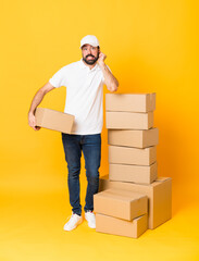 Full-length shot of delivery man among boxes over isolated yellow background frustrated and...