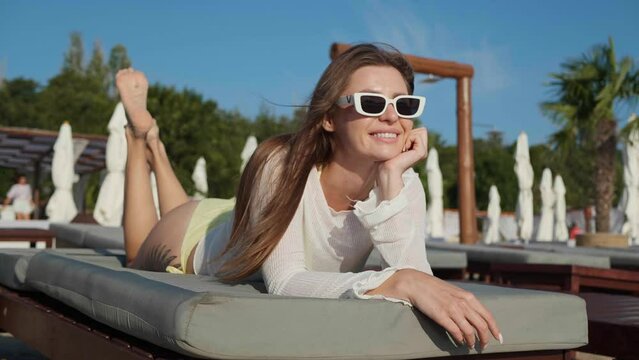 Happy woman in sunglasses resting on sunbed at resort. Camera moving, slow motion effect