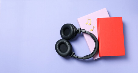 Headphones on books on purple background, space for text