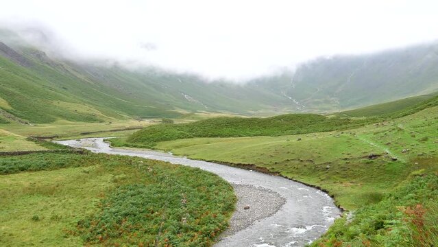 Beautiful landscape in Lake District National Park of England. Mosedale Beck mountain stream in the valley under low clouds, static elevated shot.