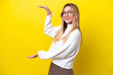Young Uruguayan woman isolated on yellow background holding copyspace to insert an ad