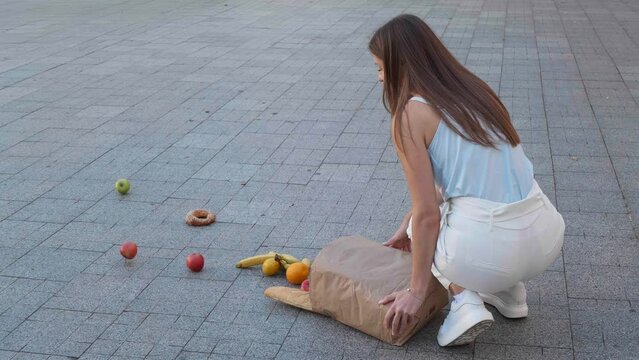 Young woman dropping paper bag of groceries outdoors