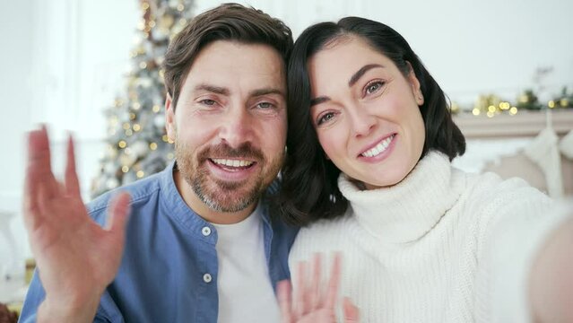 POV Webcam view. Happy family couple communicates on a video call in living room at home during winter New Year Christmas Xmas holidays. Smiling wife and husband talking wishes, congratulates remotely