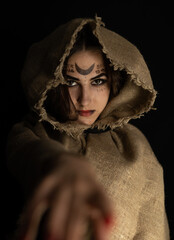 vertically. Standing in the dim Halloween light, the witch holds out her hand to the camera Looking...