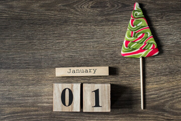 Brown wooden calendar with Christmas tree candy, mandarin, gingerbreads and anis on the dark wooden background. Christmas holidays. Reminder. 01 January, begining of year. Space for text. New Year