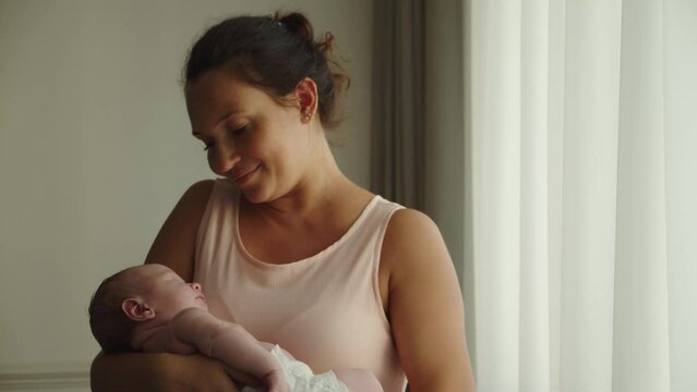 A happy mother holds a baby in her arms. A cute infant sleeps in his mother's arms. Concept of happy parenthood. Mother is rocking her newborn son in her arms. Mother and child. slow motion.