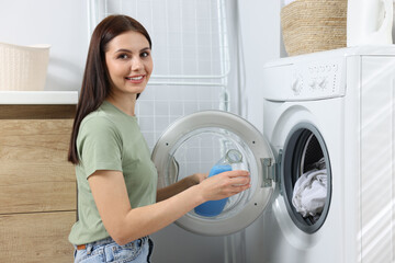 Woman pouring fabric softener from bottle into cap near washing machine in bathroom