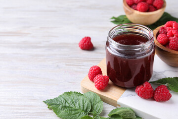 Delicious raspberry jam, fresh berries and green leaves on light wooden table. Space for text