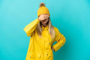 Young woman wearing a rainproof coat over isolated blue background covering eyes by hands. Do not...