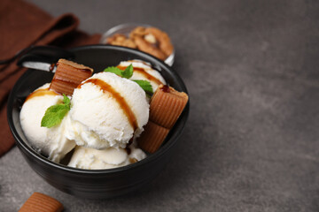 Bowl of tasty ice cream with caramel sauce, candies and mint on brown table, closeup. Space for text