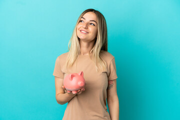 Young woman holding a piggybank over isolated blue background thinking an idea while looking up