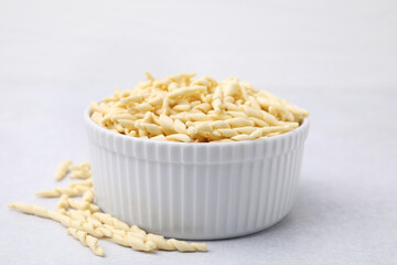 Bowl with uncooked trofie pasta on light grey table, closeup