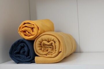 Different rolled shirts on white shelf. Organizing clothes