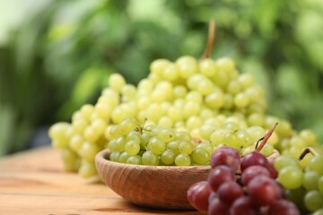 Different fresh ripe grapes on wooden table against blurred background, space for text