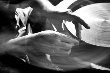 Black and white image of the hands of a young female potter throwing plates on a spinning wheel....
