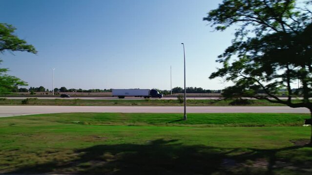 high speed side tracking a CDL Truck driver on interstate I-90 in Rockford Illinois. Commercial semi tractor Dry van - reefer. from the side with green trees in foreground.
