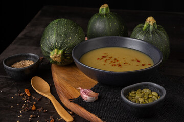 Top view of plate of zucchini puree with round zucchini, garlic, pumpkin seeds and pepper on black background, horizontal, with copy space