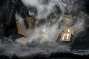Thick gray smoke descends on wooden runes on a black background	
