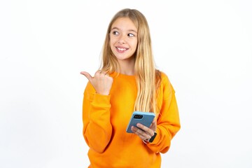 Beautiful teen girl using and texting with smartphone  pointing and showing with thumb up to the side with happy face smiling
