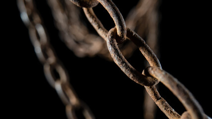 Macro shot of a rusty old metal chain on a black background. The chain links are covered in rust and dirt. Old hanging chain.