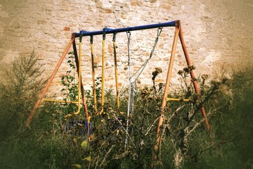 Fototapeta premium Abandoned swing in thistles in scary, grungy image