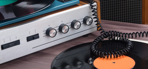 on the table there is a tape recorder for listening to music, and a stack of vinyl records, a close-up of volume controls