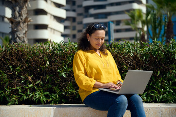 Confident purposeful businesswoman telecommuting, using laptop for remote work outdoors. People....