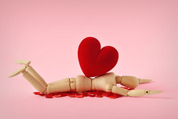 Wooden mannequin lying under heavy heart - Concept of love troubles - obrazy, fototapety, plakaty