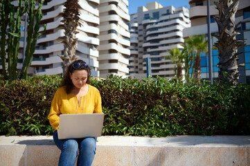 Confident purposeful female student remotely working on diploma project, sitting against modern...