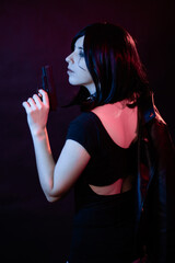 Portrait of a young woman with a bob hairstyle in a black leather jacket and a spiked collar with a gun in her hands, posing isolated on a dark background, cyberpunk concept.