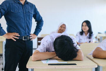 Angry teacher looking at sleeping male student in class, friends laughing on the background