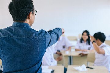 Asian male teacher angry and pointing at noisy students in classroom