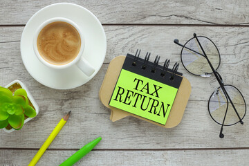Tax Return text on a bright green sticker near the glasses on the work desk. - obrazy, fototapety, plakaty