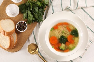 Delicious vegetable soup with noodles served on white wooden table, flat lay