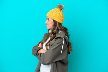 Young Italian woman wearing winter jacket and hat isolated on blue background in lateral position