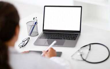Over shoulder view of woman doctor using laptop, tablet