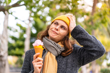 Brunette woman with a cornet ice cream at outdoors having doubts and with confuse face expression