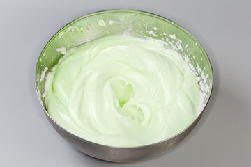 Beaten egg whites of pistachio color in stainless steel bowl
