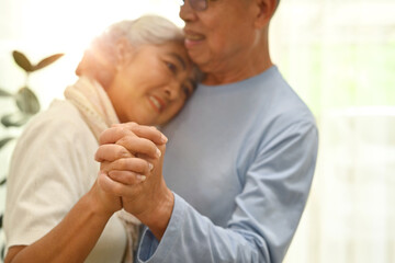 Fototapeta premium Shot of elderly couple spouses dancing in living room and looks at each other with love