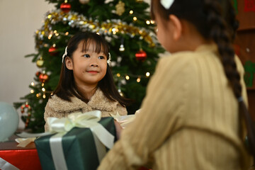 Shot of two cute little sisters exchanging Christmas gifts to each other in decorated living room