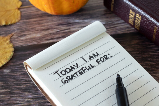 Notebook with handwritten text "Today I am grateful for", holy bible, pumpkin, and autumn leaves on wooden table. Christian gratitude list, thanksgiving to God Jesus Christ concept.