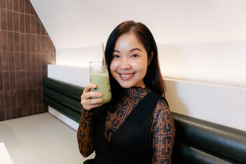 Asian woman with ice matcha in hand at cafe looking healthy